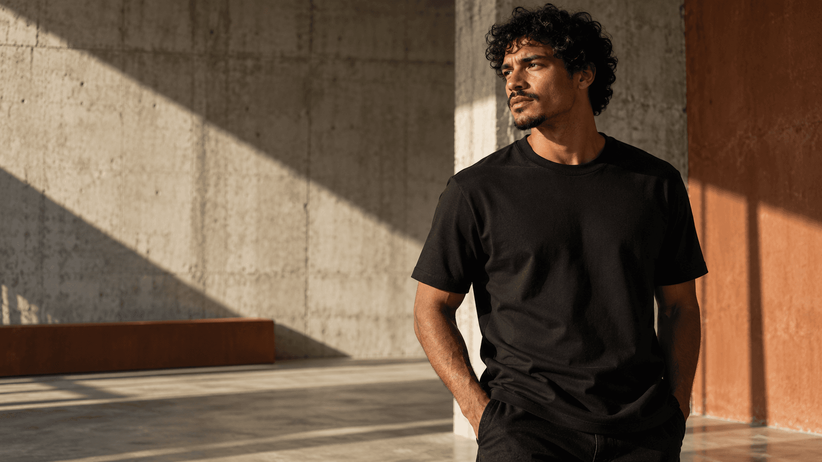 Modelo veste camiseta preta de gramatura visualmente encorpada em ambiente de concreto